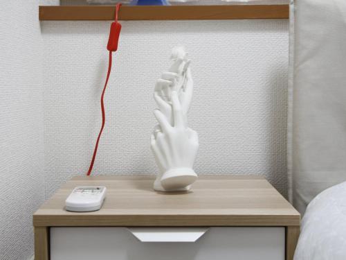 eine weiße Handstatue auf einem Nachttisch neben einer Fernbedienung in der Unterkunft Duo Scala Shinjuku 東新宿 in Tokio