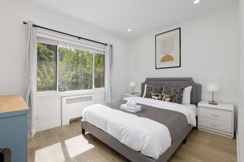 a white bedroom with a large bed and a window at Spacious Fully Furnished 2-BR Suite in Vancouver