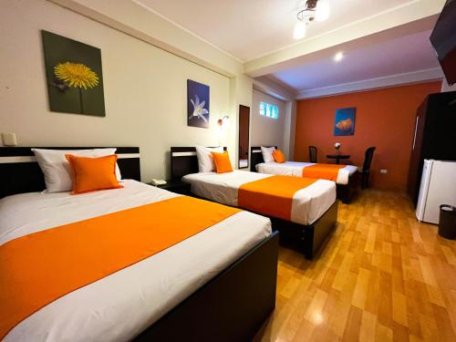 Habitación de hotel con 2 camas con sábanas de color naranja en Hotel PLATINIUM, en Tacna
