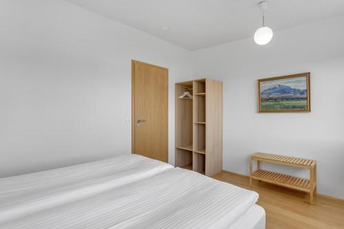 een witte slaapkamer met een bed en een stoel bij Nes Residence in Reykjavík