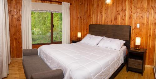 Un dormitorio con una gran cama blanca y una ventana en Cabañas Estero Loncotraro, en Pucón