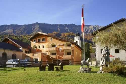 a building with a flag and a statue in a field at Hotel Landgasthof Staila in Fuldera