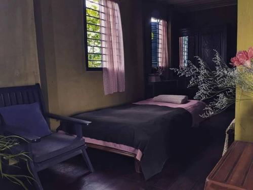 a bedroom with a bed and a chair and windows at Here Library - A wooden home by the river with a library in Thốt Nốt