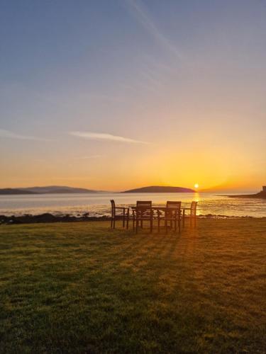 two tables and chairs in front of the ocean at sunset at Balcary Bay Country House Hotel in Auchencairn