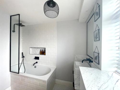 La salle de bains blanche est pourvue d'une baignoire et d'un lavabo. dans l'établissement Cosy Eton Escape with parking., à Eton