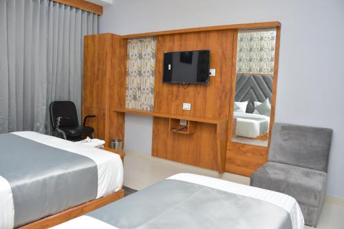 a bedroom with two beds and a chair and a tv at Hotel Green Park in Gandhinagar