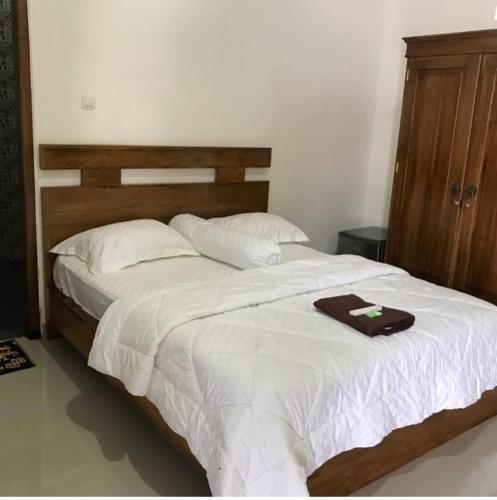 Schlafzimmer mit einem großen weißen Bett mit einem Kopfteil aus Holz in der Unterkunft Omah Joglo Pulau Merah in Pasanggaran
