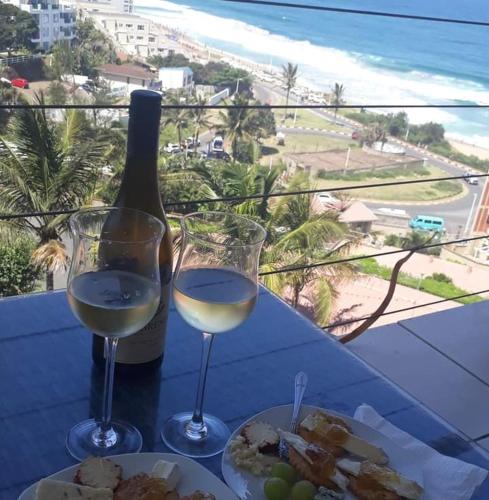 a table with two glasses of wine and a plate of food at Umdloti Holiday Resort Apartment 514 - Amazing Breaker & Ocean Views in Umdloti