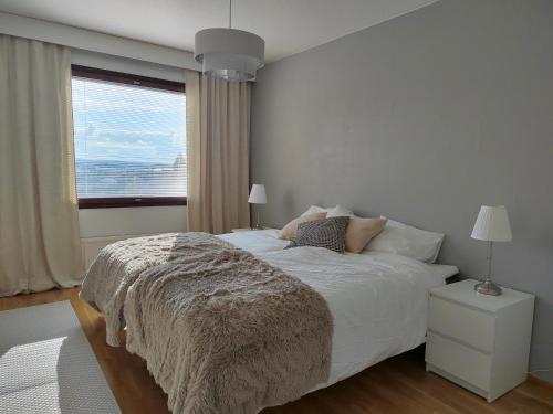 a white bedroom with a large bed with a window at City Apartment Tieva in Rovaniemi