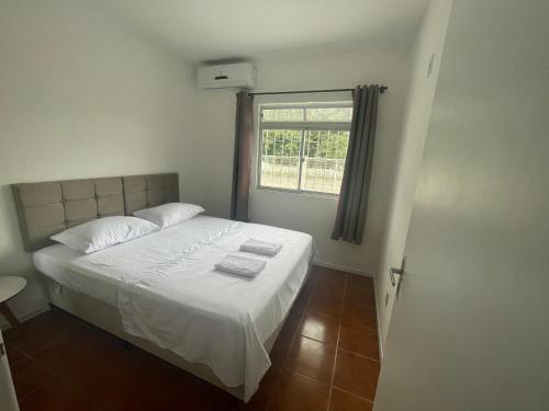 a bedroom with a bed with white sheets and a window at Residencial Mizinho in Florianópolis