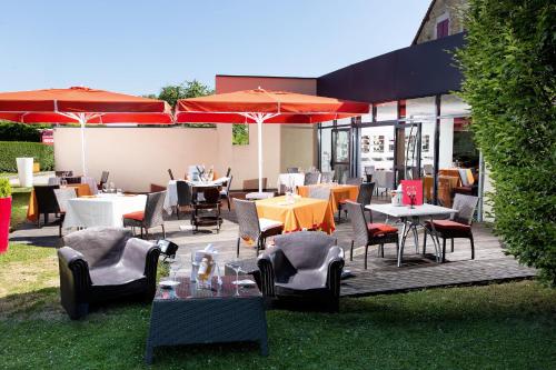 un patio al aire libre con mesas, sillas y sombrillas en Hôtel Auberge de Chavannes, en Courlans