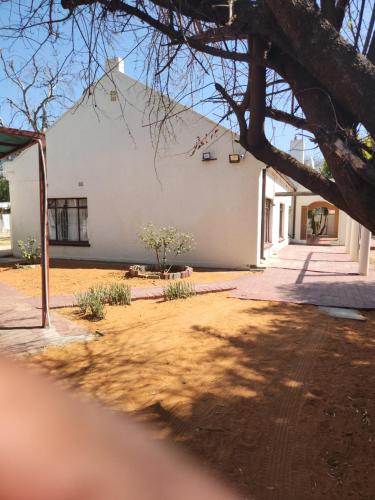 a white building with a tree in front of it at HUNTERS NEST GUEST HOUSE MAFIKENG in Mahikeng