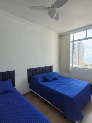 two beds in a bedroom with blue sheets and a window at Beach House 2 in Guarujá