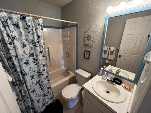 a bathroom with a toilet sink and a shower curtain at Surfside Suites in Cocoa Beach