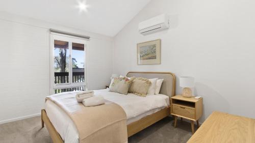 a white bedroom with a bed and a window at Treetop in Metung