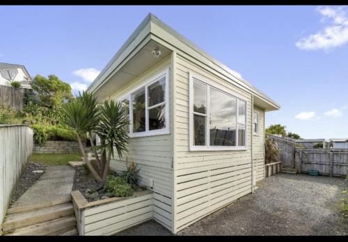 una pequeña casa blanca con 2 ventanas y una valla en Refined, Retro & Relaxing en Paraparaumu