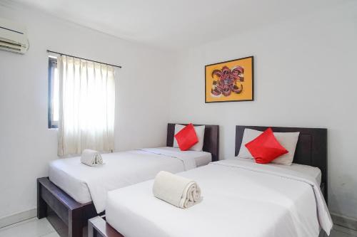 two beds in a room with white and red pillows at Gana Inn Legian in Legian
