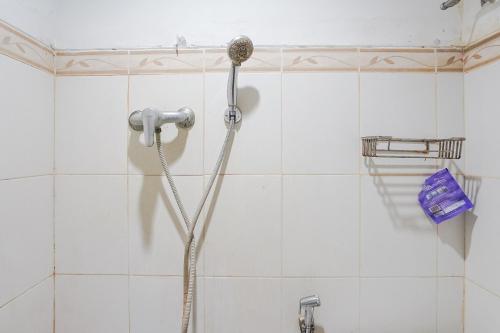 a shower head in a white tiled bathroom at Gana Inn Legian in Legian