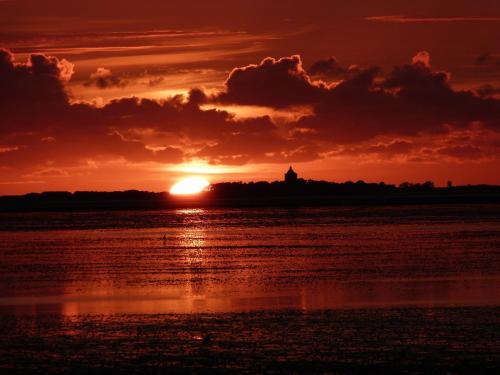 einen Sonnenuntergang über dem Wasser mit einem Leuchtturm im Hintergrund in der Unterkunft Pension Haus Erika in Cuxhaven