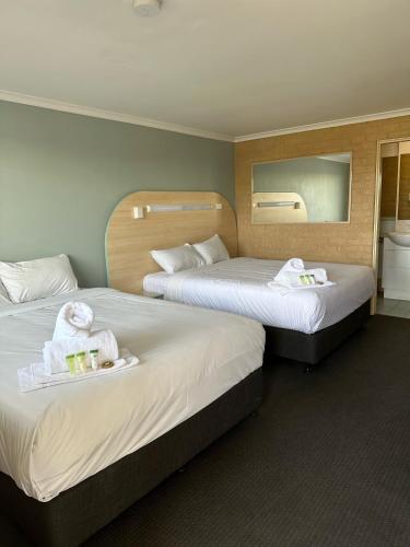 Habitación de hotel con 2 camas, toallas y espejo. en The Shamrock Hotel, en Toowoomba
