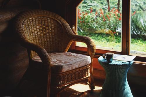 a wicker chair sitting next to a table with a coffee cup at Nhà Bao La - Hồ Đak Long Thượng in Bao Loc