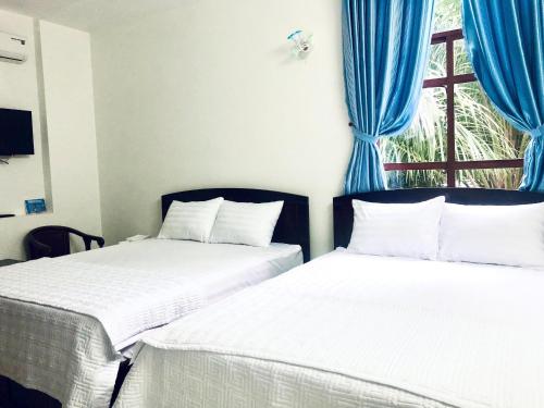 two beds in a room with blue curtains and a window at Green Ville Hotel Đồng Nai in Xa Dau Giay