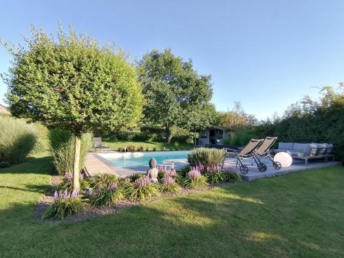 um quintal com uma piscina com uma árvore e flores em LE CLOS DU MONTYS em Louveigné