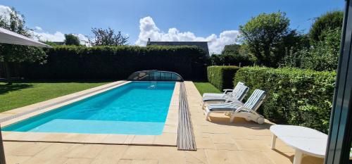 a swimming pool with two lounge chairs next to a hedge at Gîte 4 personnes avec piscine et bain nordique proche des plages du débarquement in Le Manoir