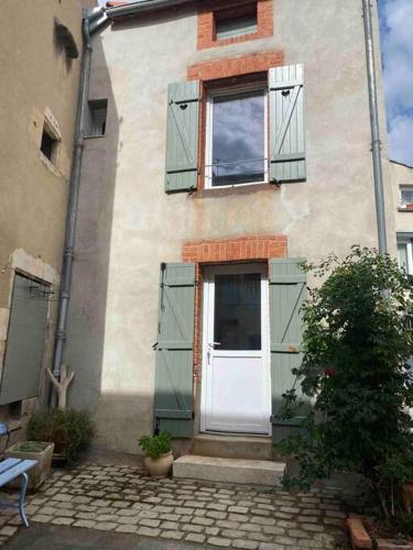 un bâtiment avec des volets verts et une porte blanche dans l'établissement Petite maison de village, à Ébreuil
