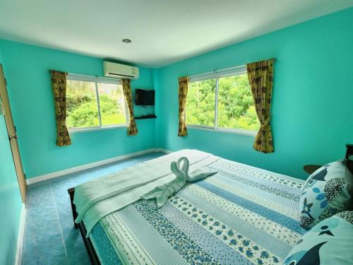 a bedroom with a bed with blue walls and windows at Blue Beach Bungalow in Bang Saphan Noi