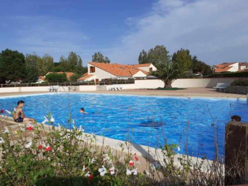 una gran piscina azul con 2 personas. en Maison avec piscine commune à 800m de la plage en Brem-Sur-Mer