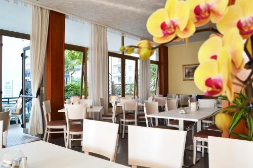 un restaurante con mesas blancas, sillas y flores en Hotel Midi, en Lido di Jesolo