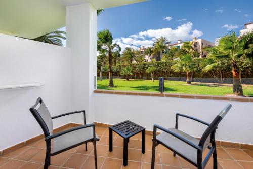 two chairs and a table on a balcony with a view of palm trees at Hotel Riu Gran Canaria - All Inclusive in Maspalomas