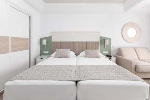 a white bedroom with a large bed and a couch at Hotel Riu Gran Canaria - All Inclusive in Maspalomas