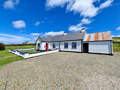 a house on a gravel lot with a driveway at Teach Róisin-Traditional Irish holiday cottage in Malin Head. in Malin