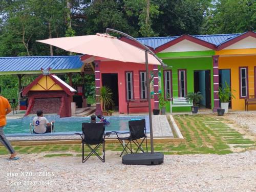 a man sitting in chairs under an umbrella in front of houses at D'DUSUN RAUDHAH HOMESTAY in Baling