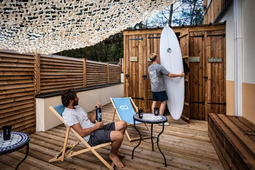 two men sitting in chairs on a deck with a surfboard at Magic Surf House in Lacanau