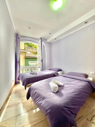 um quarto com três camas com lençóis roxos e uma janela em Habitacion privado con baño privado en La Maresía em Cudillero