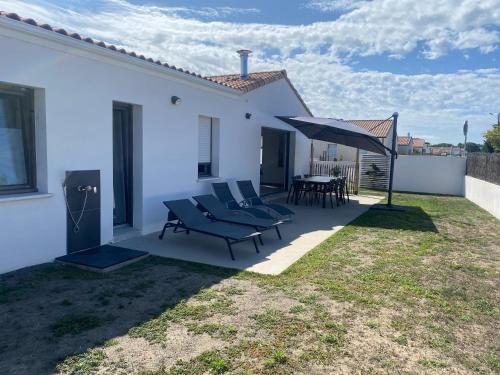 un patio avec des chaises, une table et un parasol dans l'établissement Maison en bord de mer au Domaine du Bois Soret, à Notre-Dame-de-Monts