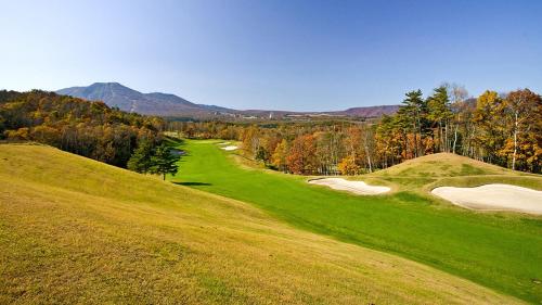 a green hillside with a golf course with trees and mountains at ANA InterContinental Appi Kogen Resort by IHG in Hachimantai
