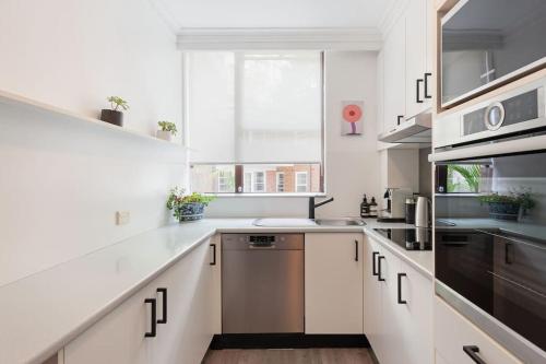 a kitchen with white cabinets and a stainless steel dishwasher at Harbourside Style, 2 Bed, A/C, Pool -Elizabeth Bay in Sydney