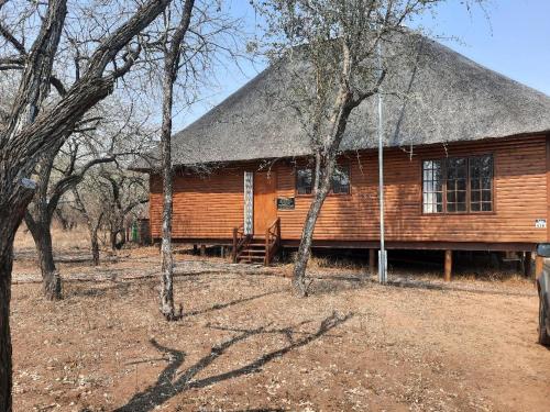 a log cabin with a thatched roof and some trees at Habibi Holiday Home in Marloth Park