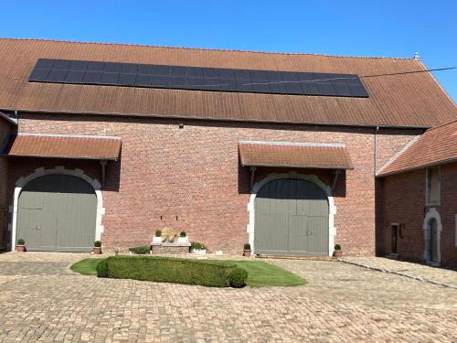 a brick building with three garage doors with solar panels at Cour 44 - Gite de charme avec sauna et jacuzzi in Remicourt
