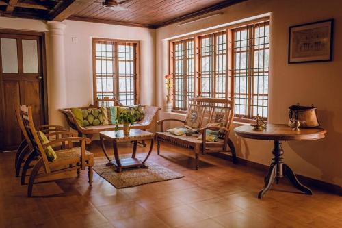 a living room with chairs and a table and windows at Meenachil Creek Homestay in Kottayam