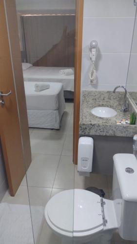 a bathroom with a toilet and a sink and a bed at Manaíra Apart Hotel in João Pessoa