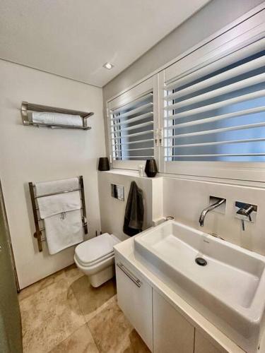 a bathroom with a sink and a toilet and a window at Clifton Beach Apartment in Cape Town