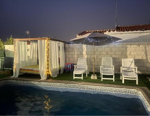 um grupo de cadeiras e um guarda-sol junto a uma piscina em La casita de los sueños em Casarrubios del Monte