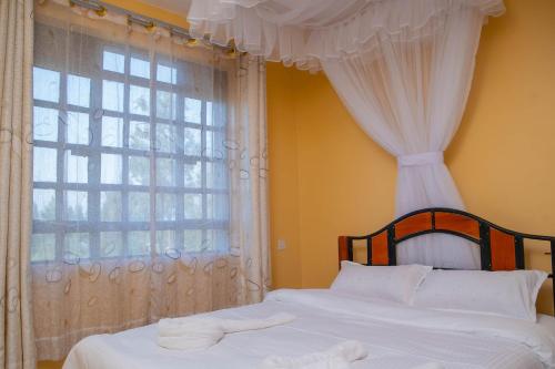 1 dormitorio con 1 cama con cortinas blancas y ventana en cla bnb en Kisumu