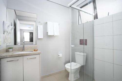 a white bathroom with a toilet and a glass shower at Boulevard Beach Canasvieiras Hotel in Florianópolis