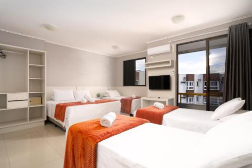 フロリアノポリスにあるBoulevard Beach Canasvieiras Hotelのベッド3台とテレビが備わるホテルルームです。